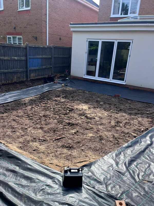 Garden groundwork preparation with weed membrane next to completed house extension