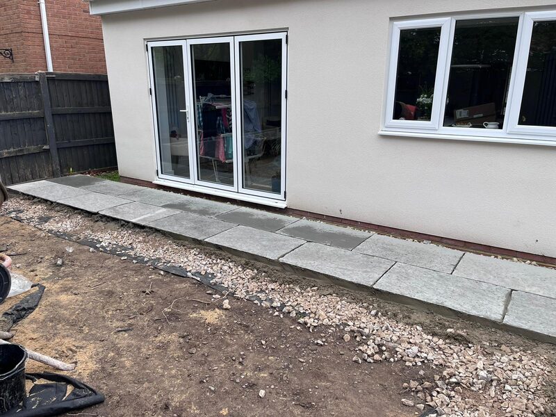 Patio slabs being laid next to rendered extension during garden groundwork