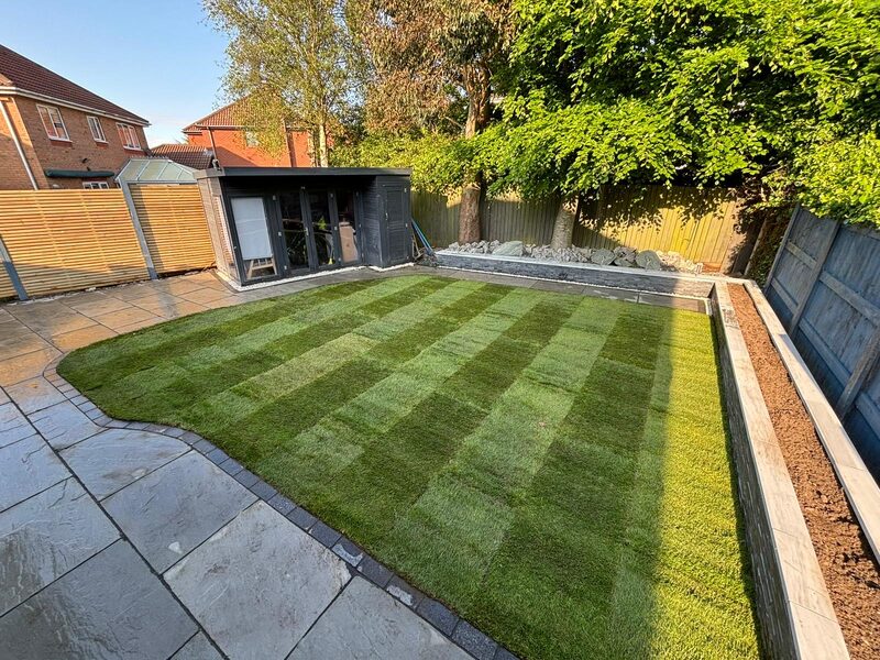Completed garden transformation with striped lawn, patio slabs and raised planter borders